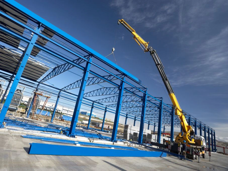 A crane lifts a steel structure at a construction site for a pre-engineered building manufacturer