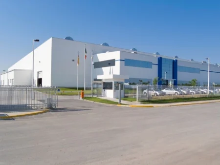 A Large White Manufacturing Building With A Fence And A Car Parked Outside Specializing In Pre Engineered Structures