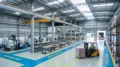 A Highly Organized Peb Factory Floor, A Forklift Moving Neatly Stacked Materials Along Marked Safety Aisles